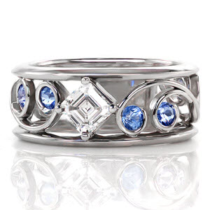 Classic filigree is paired with this modern wide band for stylish appeal. Each intricate curl is adorned with a Ceylon sapphire for a hint of color. Interwoven between the scroll patterns is a 0.50 carat asscher cut diamond. The linear parallel facets give this center stone the appearance that it goes on forever.    