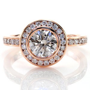 This charming rose gold design features a 1.00 carat round brilliant cut diamond in a bezel setting. The band and halo both feature channel set diamonds which keep the clean curves throughout the ring. The halo is raised up from the band to allow a traditional wedding band to fit perfectly against it. 