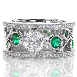 Vivid green emerald side stones are bezel set into the large scroll of the filigree pattern. The 1.00 carat radiant cut center diamond is kite-set to continue the flow of the filigree. A row of micro pavé adorns both sides of this wide band ring with milgrain texture to accent the edges. 