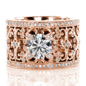 The captivating pierced pattern is adorned with micro pavé diamonds and milgrain detail. The 1.00 carat round center stone is delicately held by four spiral prongs extending from the design which are tipped with diamonds. Two rows of bead set diamonds border the design to add exquisite brilliance.