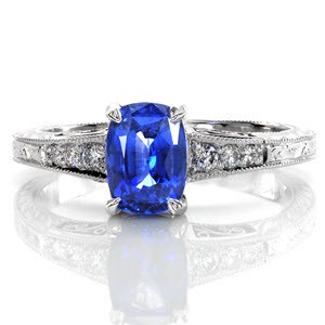 The vibrancy of the 1.20 carat blue sapphire is heightened by the round brilliant diamonds along the band. The artistic details of hand engraving and platinum filigree curls embraces an old world charm. This antique inspired design is textured with milgrain along each edge for a radiant finish.  