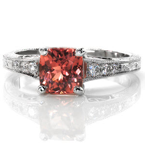 The 1.00 carat cushion cut Padparadscha Sapphire in this design is mesmerizing with its rare, luscious color. The tapered band has tantalizing details to compliment the center stone; the filigree and side stones near the top and the splendid hand engraving below. 
