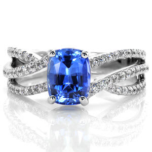 Grasped by four classic prongs, a 1.50 cushion cut blue sapphire floats above the delicate waves of micro pavé diamond bands.  The Adriana Sophia design incorporates three 14k white gold interlaced bands. With a high polish finish, the bands merge at the bottom of the shank for a comfortable fit.