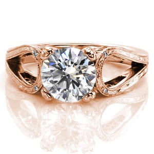 This design is as unique as it is breathtaking. The 1.70 carat round brilliant center diamond is nestled between a split shank band that loops instead of merging with the center setting. The top of the band is enthralling with hand engraving and a few surprise diamonds and the sides have filigree.