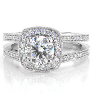 A 1.0 ct round diamond is held in a four prong setting and accentuated with micro pavé  diamonds set in a soft square halo. The design features a double band look with two rows of bead set diamonds. Two round bezel set diamonds are hidden beneath the halo, embellished by hand cut engraving. 