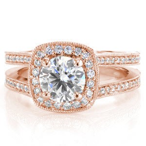 A 1.0 ct round diamond is held in a four prong setting and accentuated with micro pavé  diamonds set in a soft square halo. The design features a double band look with two rows of bead set diamonds. Two round bezel set diamonds are hidden beneath the halo, embellished by hand cut engraving. 