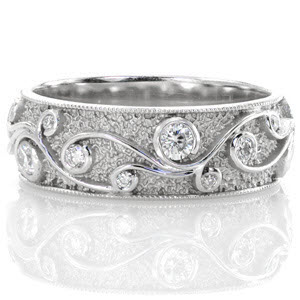 The Cirrus design frames beautiful scroll filigree curls which capture varying sizes of round cut diamonds. The hand stippling on this design makes a wonderful background to the high polished turns of filigree. The domed band is finished with edges of milgrain.