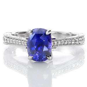 The magnetic color of this 1.50 carat cushion cut sapphire is a perfect focal point on this graceful, vintage-inspired ring. The top of the band is adorned with bead set diamonds while the sides are handsomely appointed with hand engraving, filigree, and three petals with diamonds delicately placed.