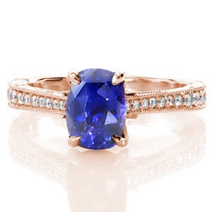 The magnetic color of this 1.50 carat cushion cut sapphire is a perfect focal point on this graceful, vintage-inspired ring. The top of the band is adorned with bead set diamonds while the sides are handsomely appointed with hand engraving, filigree, and three petals with diamonds delicately placed.