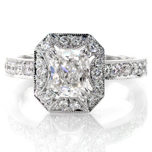 This glamorous design is shown with a 1.00 carat cushion cut center diamond in a claw prong setting. The halo has a unique starburst pattern cut-out around the center stone. The top of the band and the halo are exquisitely adorned with micro pavé and edged in milgrain for a refined finish.