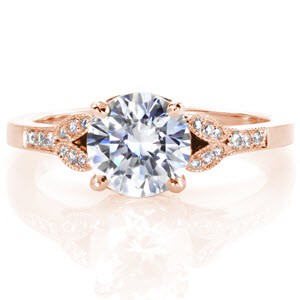 The 1.00 carat center stone is prominently displayed in a four prong basket setting. Petal details flowing down the ring are accentuated with micro pavé diamonds and a milgrain beaded edge. The hand wrought filigree curls, created by our master jewelers, detail two windows adding graceful detail.   