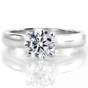 This classic solitaire design features a sleek wide band and a 1.00 carat round brilliant center diamond. The side profile reveals a beautiful row of micro pavé surprise diamonds at the base of each side of the center stone. The prongs extend and curve down to meet the bridge of the band. 