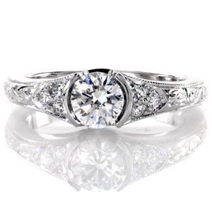 This charming design features a 0.60 carat round brilliant cut center diamond in a half bezel setting. The band tapers slightly and elegant hand engraving adorns the top of it up to a cluster of micro pavé on each side of the center stone. The edges of the band have a milgrain texture.