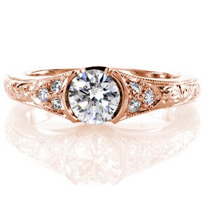 This charming design features a 0.60 carat round brilliant cut center diamond in a half bezel setting. The band tapers slightly and elegant hand engraving adorns the top of it up to a cluster of micro pavé on each side of the center stone. The edges of the band have a milgrain texture.