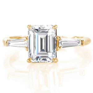 Henderson classic custom engagement ring on a slim polished band with an emerald cut diamond center bordered on either side by a tapering banquette diamond.