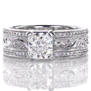 This stunning design features a very wide band with a 1.00 carat radiant cut center diamond. There is a row of micro pavé accenting each edge of the band with a row of hand engraved patterns in the middle. The engraving is a raised, relief style with the design being higher than the background. 