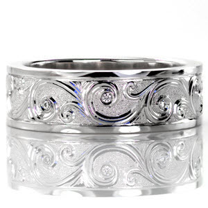 Continual scrolls grace the surface of Design 2487. The unique hand engraved style displays a raised relief in which each of the scroll designs are higher than their background. Perfectly placed round cut diamonds are flush set within the larger curls.