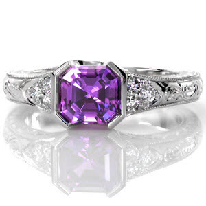 The striking 1.30 carat asscher cut natural purple sapphire is set perfectly within Design 2492. The half bezel design is complimented by round diamond side stones. The hand engraved band displays fine milgrain edges. Four pockets within the 14k white gold band frame intricate hand wrought filigree scrolls.