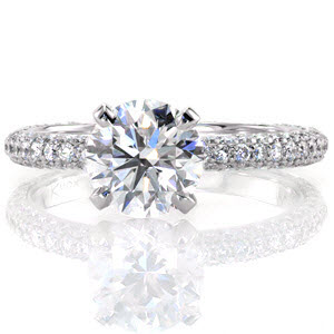 This ravishing design features a 1.50 carat round brilliant center stone which is elevated above the band in a traditional four prong setting. The center diamond is raised to allow a wedding band to sit flush next to this engagement ring. The band of this piece is luxuriously adorned with three rows of micro pavé.