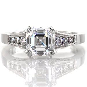 This elegant design features a 1.73 carat asscher cut center diamond in a double prong setting. The tapered band has channel set round diamonds on either side of the center stone and micro pavé on the prongs. There are stunning handmade filigree curls visible from the side profile of this ring.