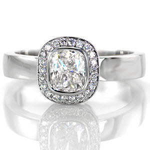Crafted in 14k white gold, Design 2543 has a high polish streamlined band. The 1.00 carat cushion cut center diamond has a crisp full bezel which is surrounded by a halo of round cut diamonds and finished with hand applied milgrain on halo outer edge. This is a lustrous contemporary design.