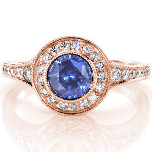 This design is magnetic with its luscious 1.00 carat round cut blue sapphire. The halo and tapered band are adorned with micro pavé and edged with milgrain texture for a refined finish. The side profile shows off stunning hand engraving and hand made filigree curls.