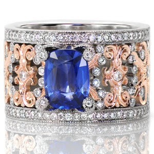 This stunning piece is crowned with a 1.60 carat cushion cut blue sapphire. The prongs holding the center stone each have a bezel set diamond on top. This mesmerizing two-tone wide band is made in 14k white and rose gold with a euro shank for a signature look. The details of the ring are accented with micro pavé