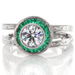 This magnificent design is exquisitely hand crafted with a platinum, split shank band adorned with mesmerizing hand engraving. The center is a bezel set 0.75 carat round brilliant cut diamond surrounded by a micro pavé emerald halo. The basket of the halo has filigree and bezel set surprise diamonds.