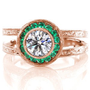 This magnificent design is exquisitely hand crafted with a platinum, split shank band adorned with mesmerizing hand engraving. The center is a bezel set 0.75 carat round brilliant cut diamond surrounded by a micro pavé emerald halo. The basket of the halo has filigree and bezel set surprise diamonds.