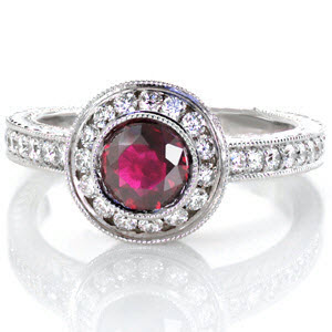 The Ruby Monarch is an enthralling design with a luscious 1.00 carat round ruby center. The center stone is bezel set and surrounded by a halo. Both the halo and band are adorned with micro pavé, with hand engraving on the band and filigree and a bezel set surprise diamond on the basket of the halo.