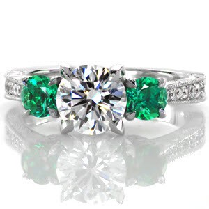 Glowing green emeralds makes this three stone ring a statement piece. A 1.00 carat center diamond is proudly accented over a lotus style petal design with diamond embellishments. Hand engraving and micro pavé diamonds along the shank add the finishing touches to this stunner. 