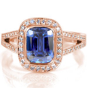 The royal blue of the 2.00 carat cushion cut sapphire is a signature statement of regal expression. Round diamonds outline the sapphire to embellish the beautiful blue of the center stone. The split shank cathedral is lined with bead-set diamonds and accented with two bezel set stones for a majestic finish.  