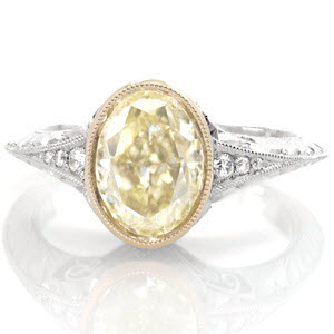 This vintage inspired design puts all attention on the luscious 2.00 carat oval cut fancy yellow diamond center stone. The center is set in an 18k yellow gold bezel to compliment the color of the diamond. The band is fashioned in platinum with a knife edge. The hand formed filigree curls and engraving are mesmerizing. 