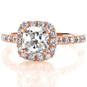 Micro pavé diamonds outline the shape of the 1.20 carat cushion cut center stone. The u-cut settings use less metal to securely fashion the round diamonds maximizing the brilliance and sparkle of each stone. Double claw prongs fashion the center adding a simplistic detail to the corners of the cushion.