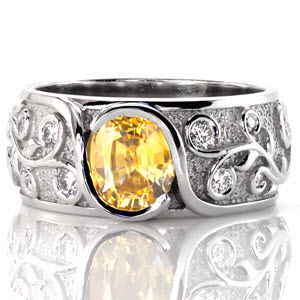 The edges of this interwoven design wrap up and around a bright yellow sapphire, cradling the cushion center in a bezel fashion. Relief engraving of the vines artistically spiral around the shape of a round brilliant diamond. The stipple background adds texture and contrasts the raised high polish engraving. 