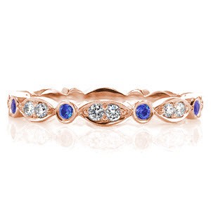 Design 2823 is an eternity band crafted in 14k white gold. Alternating stations of round cut bezel set blue sapphires are accented by a marquise shape pattern with two bead set round brilliant diamonds. The high polish finish accents the vibrancy of the natural blue sapphires and white diamonds.