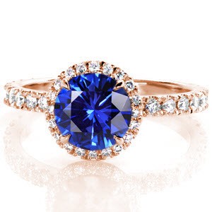 This stunning engagement ring catches the eye with an elegant cobalt blue sapphire center stone. Round brilliant diamonds are set into the underside of the halo to ensure that the piece will catch the light from every angle. The classic diamond band compliments the setting and highlights the center stone.