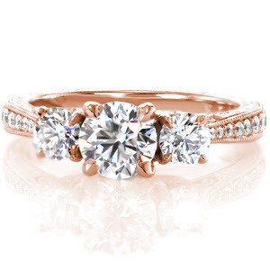 This breathtaking design uses antique inspired details to create an elegant ring. The band tapers as it reaches the three center stones and the top is adorned with bead-set diamonds. The side of the piece reveals marquis shaped petals supporting the center stones. Hand engraving and filigree complete the design.