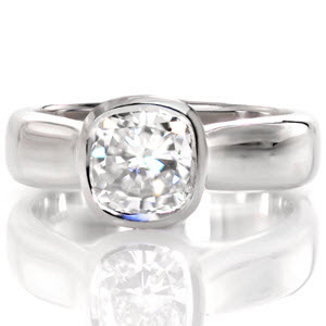 The Cashmere is a sleek, contemporary engagement ring with a wide tapered band. The 1.00 carat cushion cut center diamond is featured in a bezel setting on top of a woven trellis pattern visible from the sides of the piece. The luster of the high polished metal adds elegance to this beautiful ring.