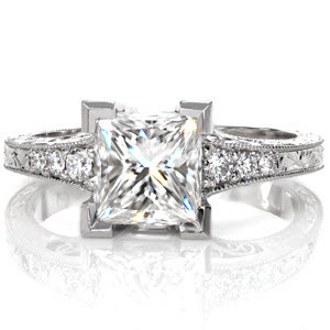 Design 2885 joins the vintage styling of engraving and hand crafted filigree with a stunning 1.50 carat Princess cut diamond. Chevron prongs create the most secure setting and the flared band is accented by graduated round cut diamonds. Hand applied milgrain and detailed under gallery add the perfect finishing touch.