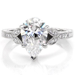 A 1.50 carat pear cut diamond is the focus of this antique inspired engagement ring. The split shank of the band takes the form of two delicate leaves supporting the center stone. The band is detailed with elegant hand formed filigree curls and hand engraving. A beaded milgrain texture has been added to the edges.