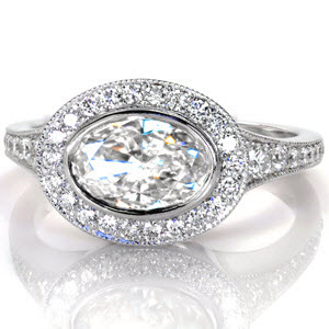This stunning contemporary design features a bezel set oval center stone turned lengthwise across the finger. The flared band features diamonds graduating in size to blend into the ends of the brilliant micro pave halo. The high polished sides of the ring offer a contemporary feel of sleek elegance.