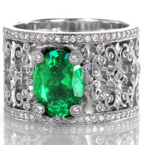 Emerald Caledonia is a stunning example of sophisticated artistry. Ornate diamond topped prongs surround a natural oval cut emerald. Broad filigree flourishes curl and hold bezel set round cut diamonds. Each turn of metal has hand applied milgrain detail to enhance a vintage look.