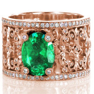 Emerald Caledonia is a stunning example of sophisticated artistry. Ornate diamond topped prongs surround a natural oval cut emerald. Broad filigree flourishes curl and hold bezel set round cut diamonds. Each turn of metal has hand applied milgrain detail to enhance a vintage look.