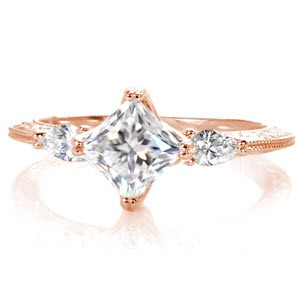 This elegant three stone diamond engagement ring is breathtaking with a kite-set princess cut center diamond. The antique inspired knife edge band flows beautifully down from the points of the pear cut side stones. This unique engagement ring is exquisitely detailed with relief-style hand engraving and milgrain.