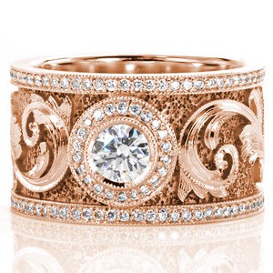 An elegant motif drapes across this signature band. A 0.50 carat bezel set center is accented with a micro pavé halo. The scroll work along the band is magnificent with hand engraved detail and faceted stipple background that captures the light. Two rows of milgrained micro pavé diamonds frame the design. 