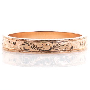 This antique inspired wedding band is handcrafted in 14k rose gold. Hand engraved scroll patterns extend along the entire band for a continuous look. Milgrain texture is applied to the edges of the design to add dimension and complete its vintage appeal.