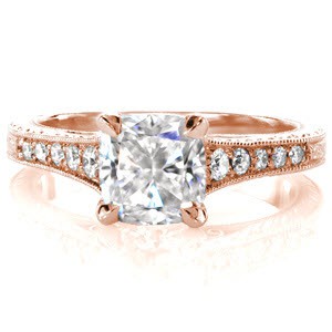 This antique inspired design is handcrafted in 14k white gold. A 1.00 carat cushion cut center stone is magnificently framed in a four prong setting. Tapered diamonds along the band is met by an elegant scroll engraved pattern. The side profile reveals hand-wrought filigree and a half-wheat engraved pattern. 