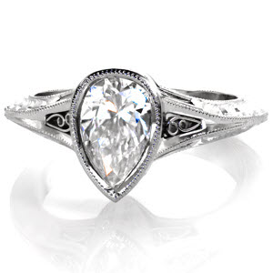 Design 3060 is a charming ring featuring a bezel set 0.80 carat pear-cut diamond on a knife edge band. The central diamond is framed by filigree curls on either side leading into a tapering , double milgrain edge band. The profile of the band includes hand engraved, hard-formed filigree and surprise diamonds.