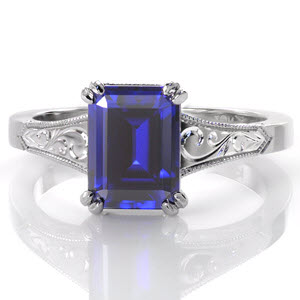 Gorgeous sapphire engagement ring in Miami. This luscious blue emerald cut sapphire is featured in an antique engagement ring style with hand engraved scroll patterns on the top and sides of the band. The sides of this unique engagement ring also feature delicate, hand formed filigree curls for vintage appeal.